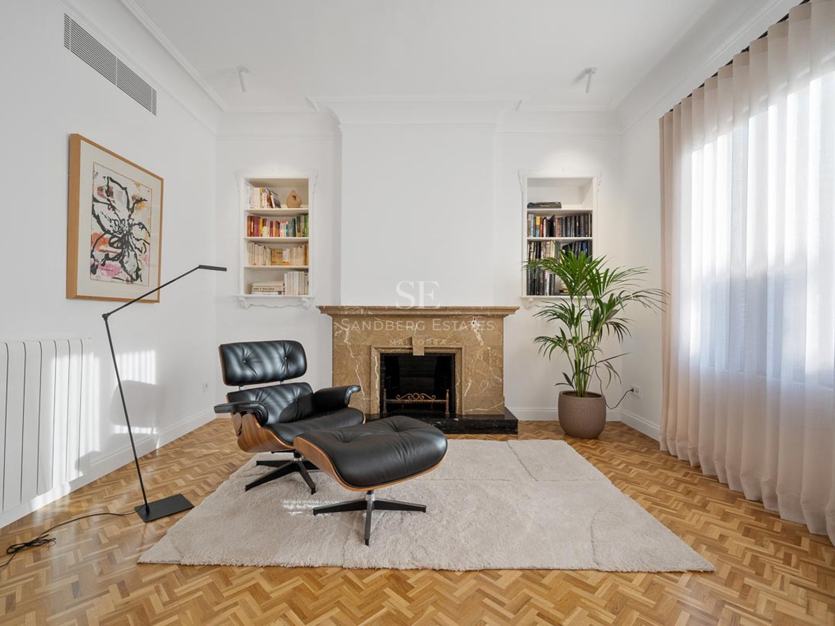 Salon moderne avec fauteuil Eames en cuir, cheminée en marbre, parquet et étagères intégrées.