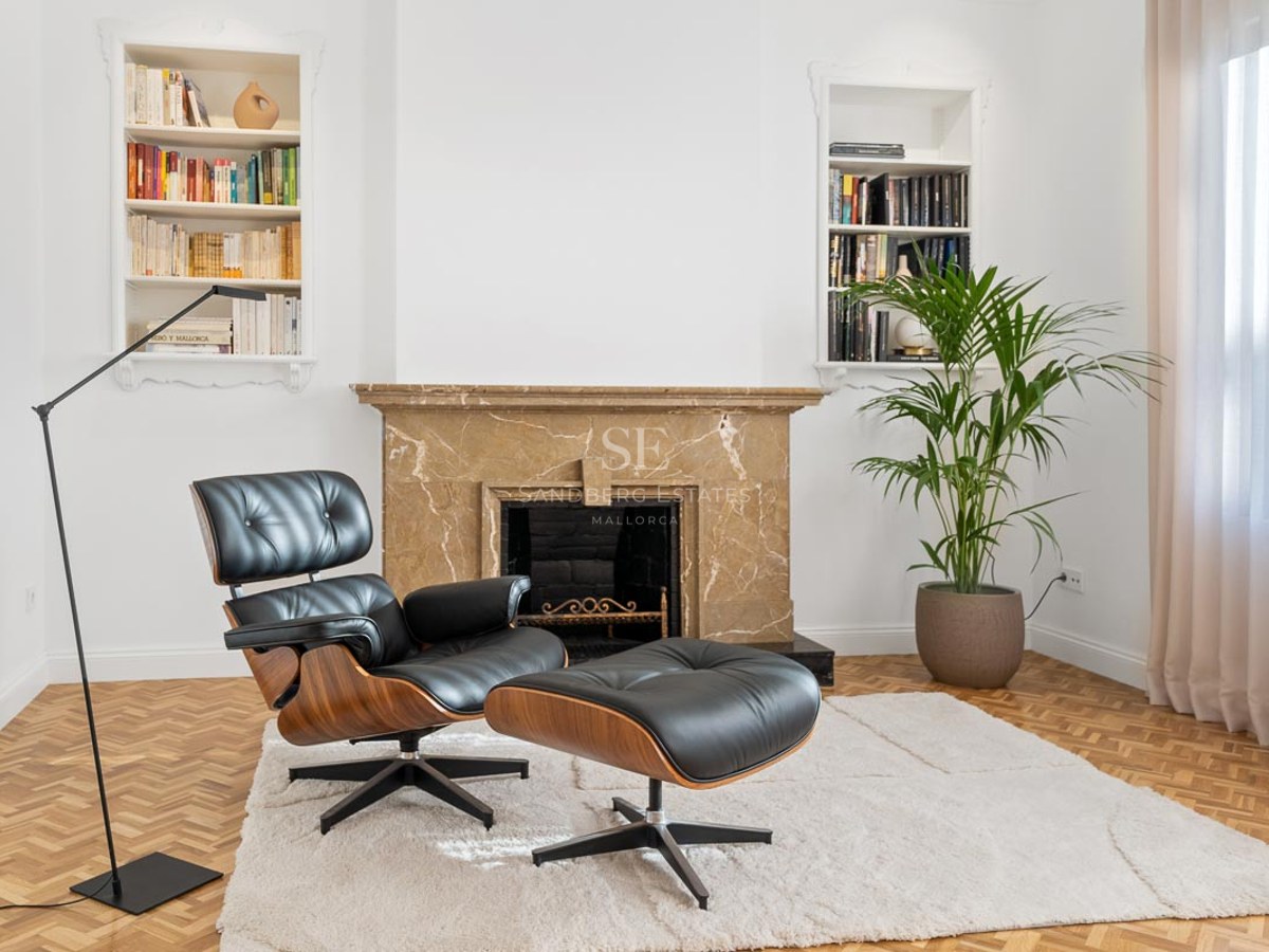 Fauteuil en cuir noir et repose-pieds devant une cheminée en marbre et des bibliothèques encastrées.