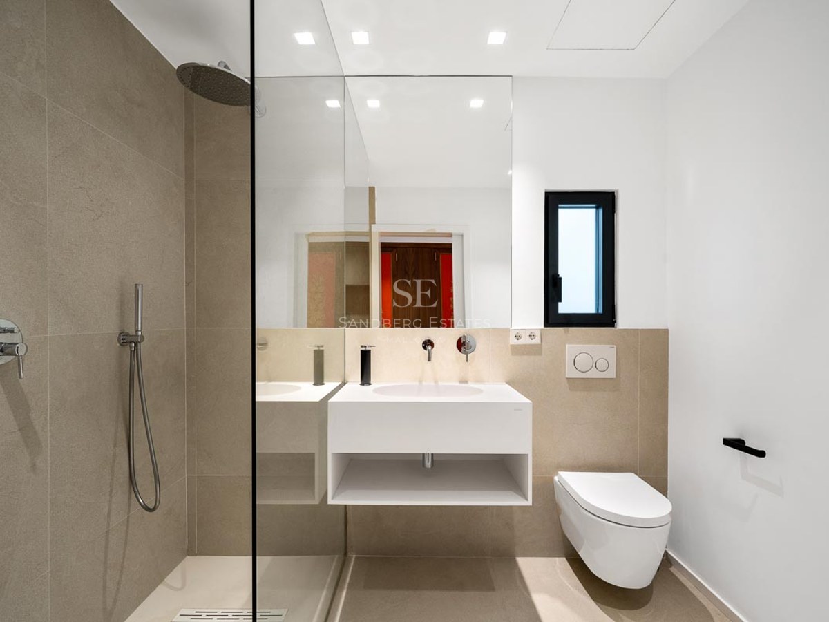 Salle de bain moderne avec douche à l'italienne vitrée, vasque suspendue blanche et carrelage beige.
