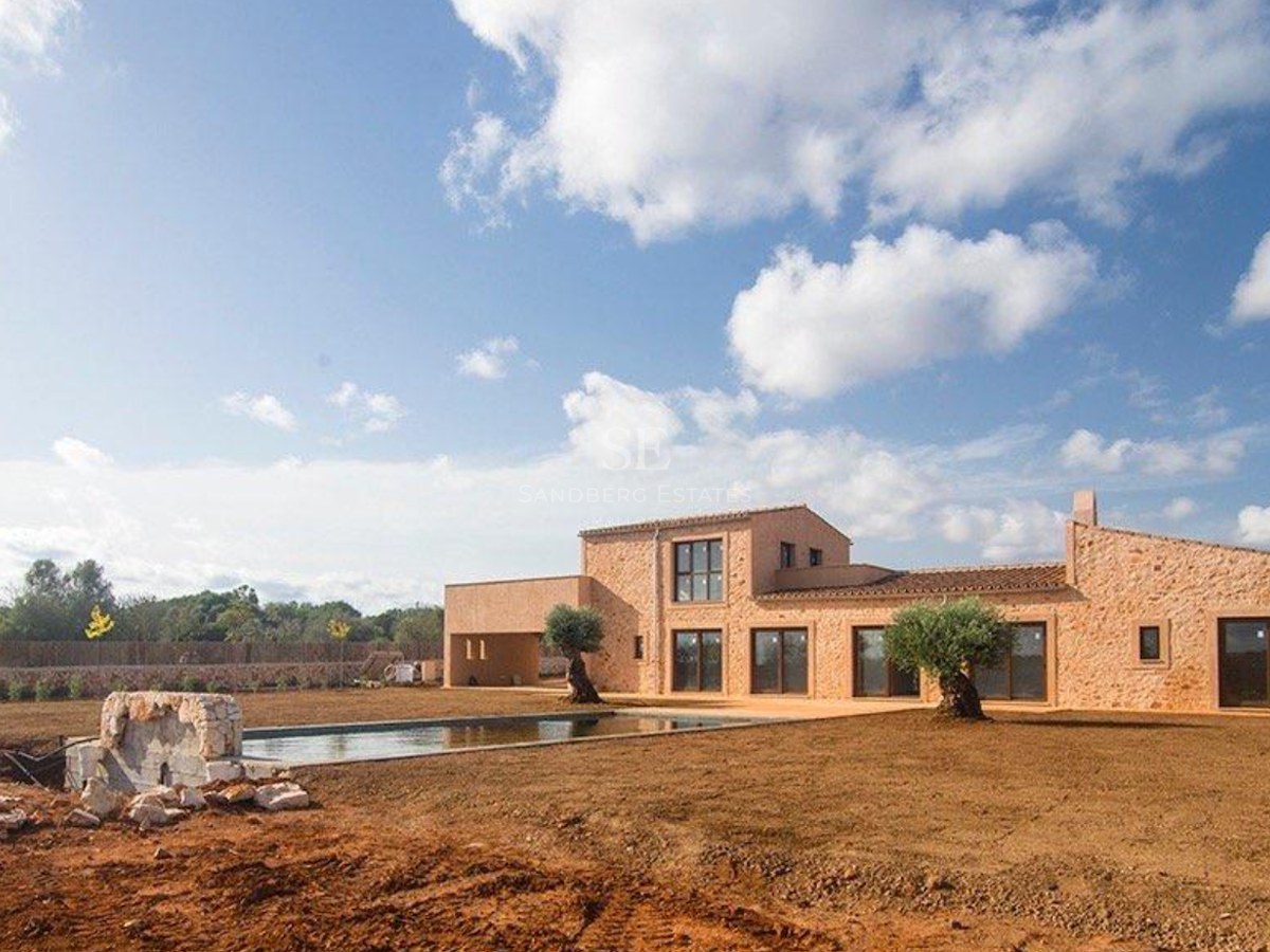 Natural stone facade of a modern villa with a swimming pool and olive trees under a bright blue sky.