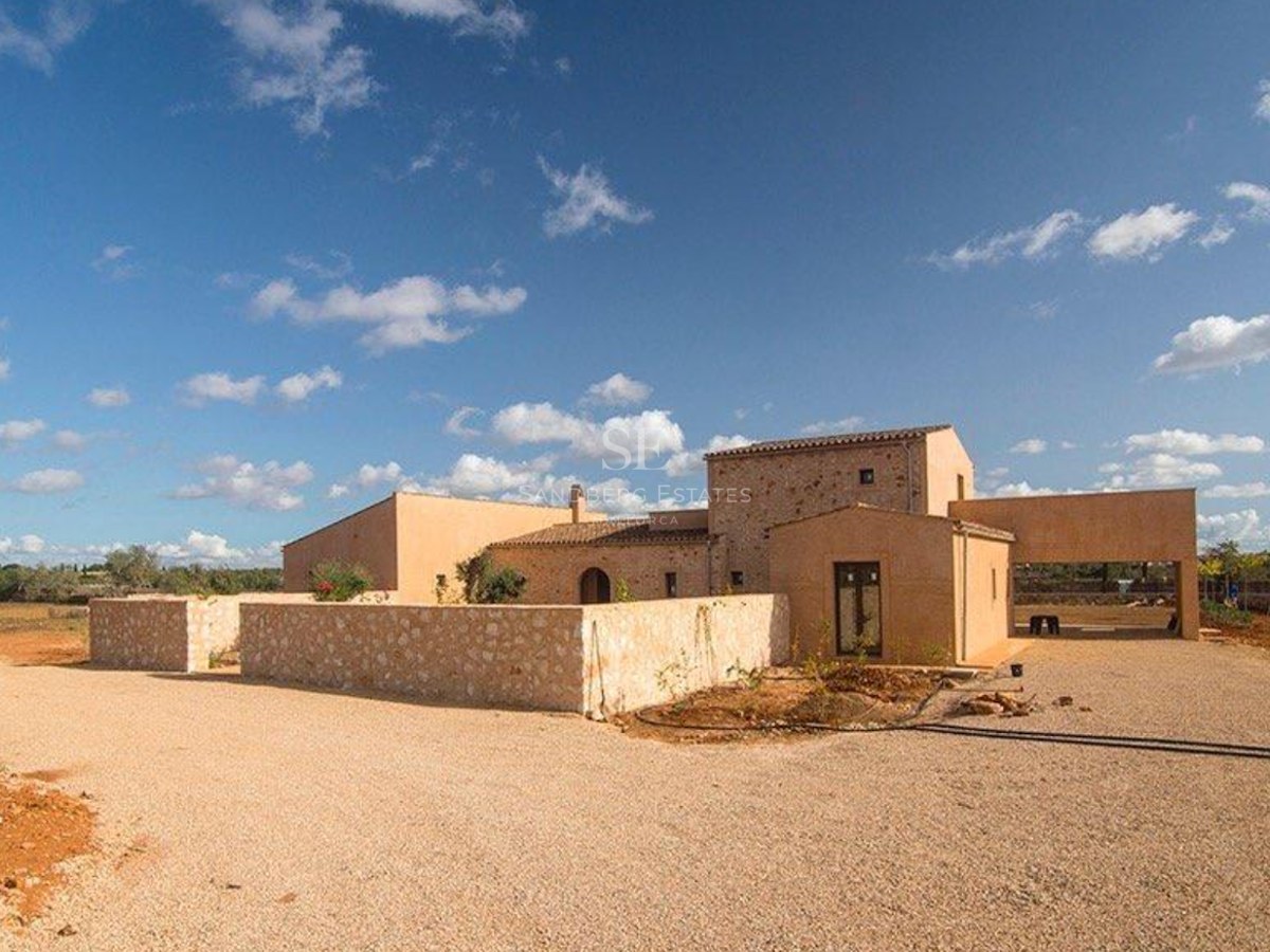 Exterior view of a modern Mediterranean stone villa with ochre walls, gravel driveway, and clear blue sky.