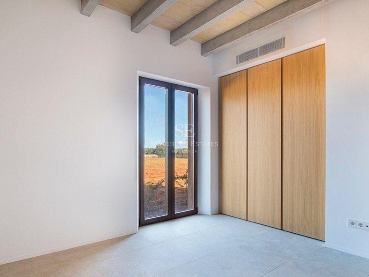 Bright bedroom with wooden ceiling beams, built-in oak wardrobes, and a window overlooking a rural landscape.