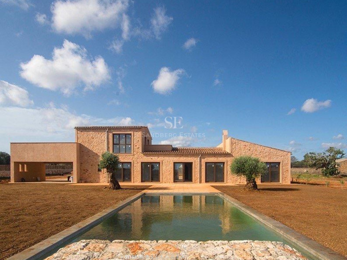 Exterior view of a natural stone villa featuring a rectangular swimming pool, olive trees, and large windows.