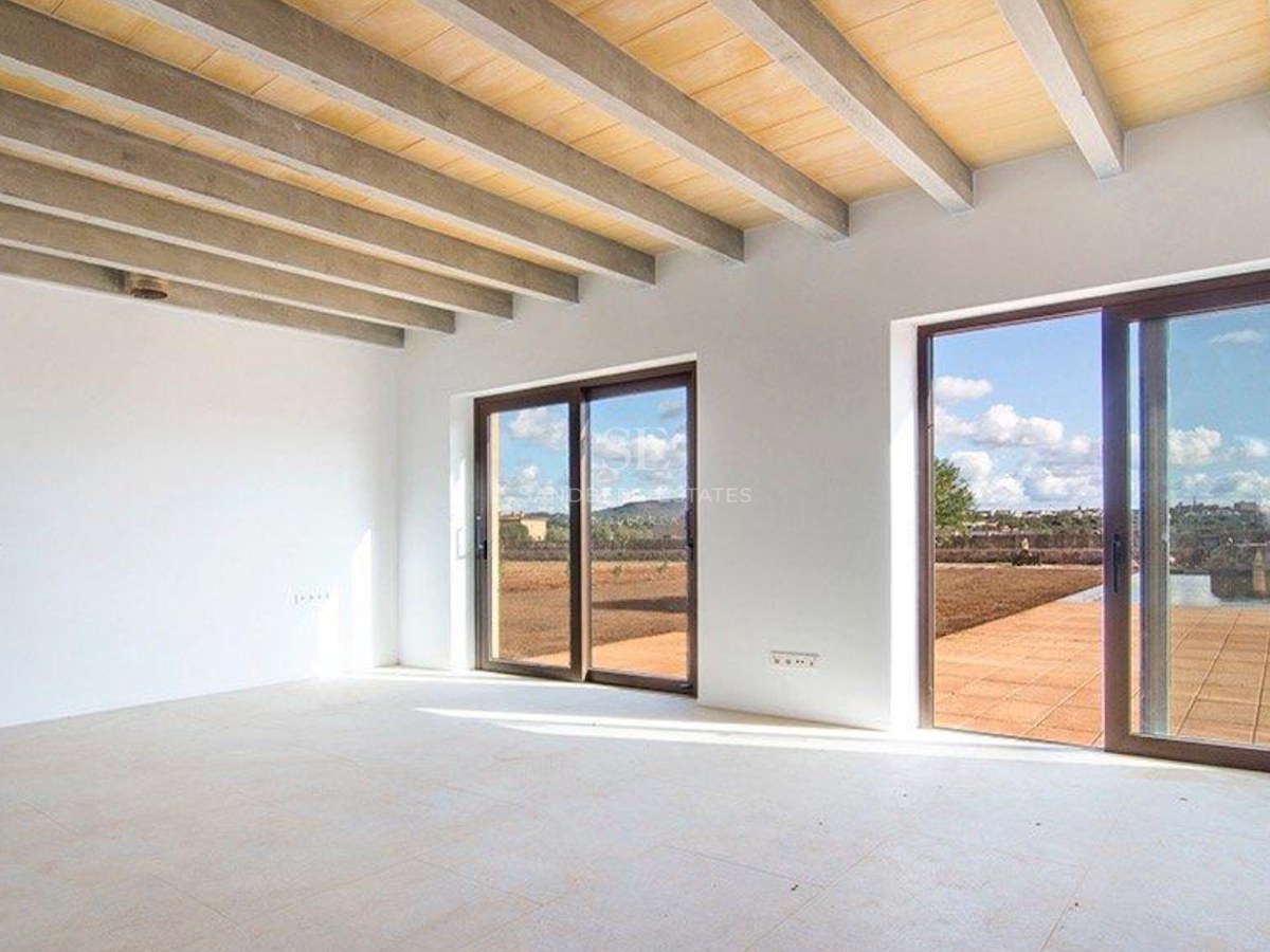 Spacious empty room with exposed concrete and wood ceiling beams, white walls, and sliding glass doors to a terrace.