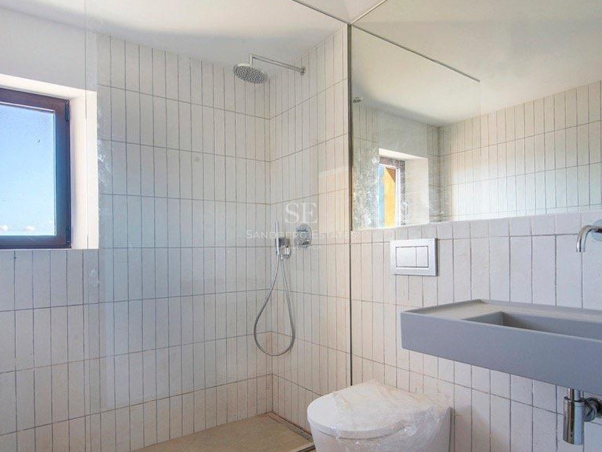 A modern bathroom with white vertical tiles, a walk-in shower, a grey floating sink, and a large wall mirror.