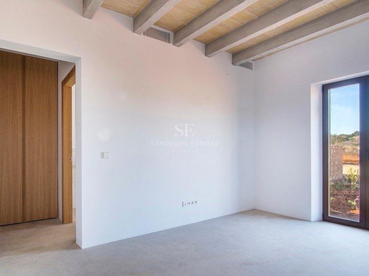 Empty bedroom featuring white walls, exposed wooden ceiling beams, built-in oak wardrobes, and a glass door to the exterior.