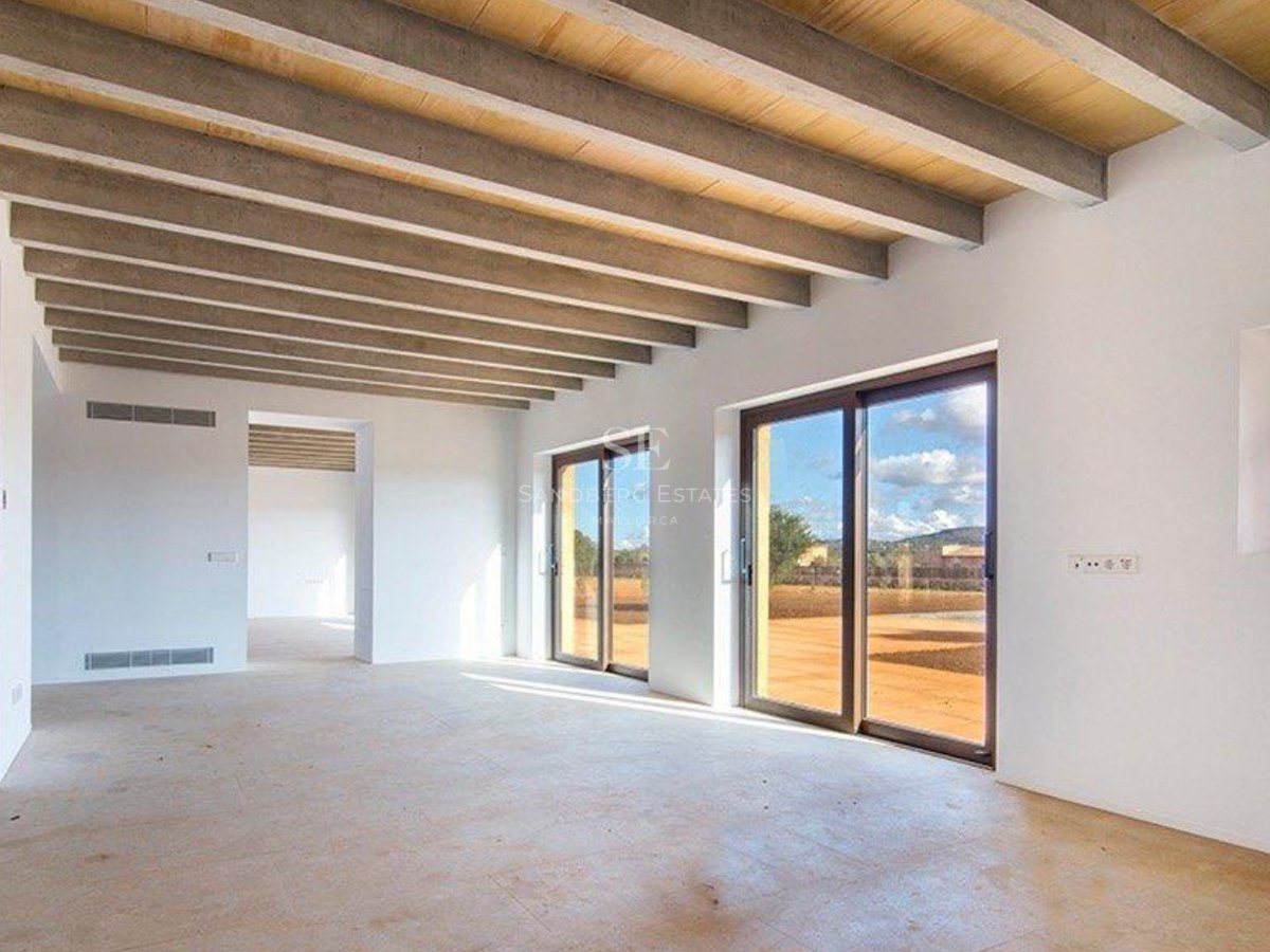 Spacious unfurnished living room featuring exposed ceiling beams, large sliding glass doors, and light stone flooring.