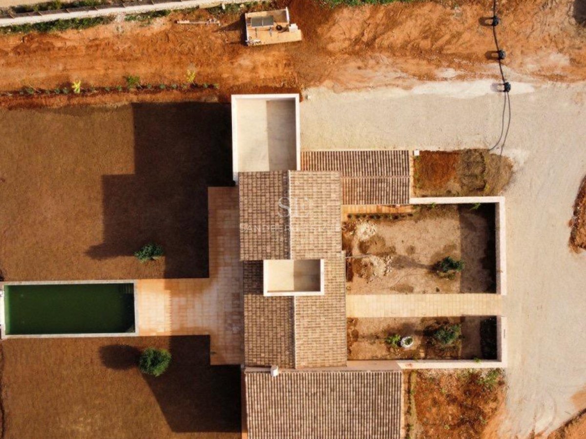 Top-down drone shot of a modern villa featuring tiled roofs, a rectangular pool, and courtyards under development.
