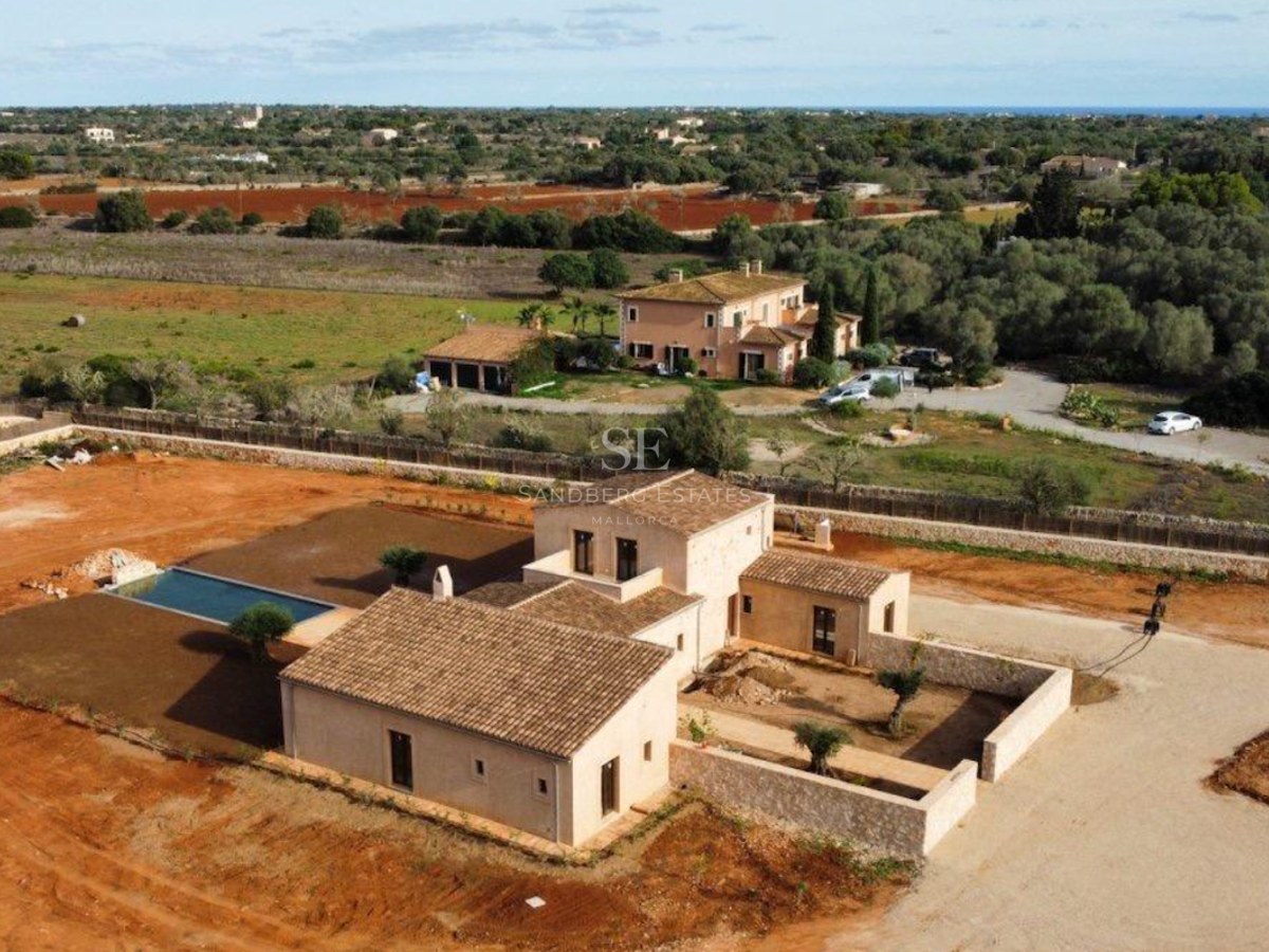 Aerial view of a large traditional Mallorcan villa with a swimming pool and stone walls under a clear sky.
