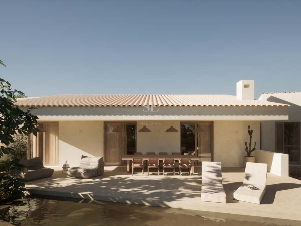 White plastered terrace featuring a long wooden dining table, lounge seating, and pool edge under a clear sky.