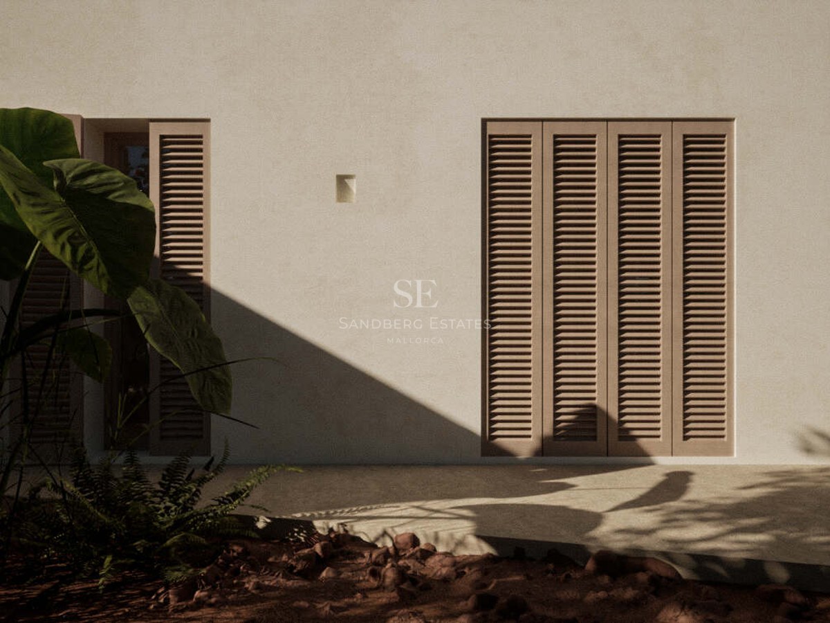 Sand-toned stucco exterior wall featuring closed louvered shutters and tropical foliage in the foreground shadows.
