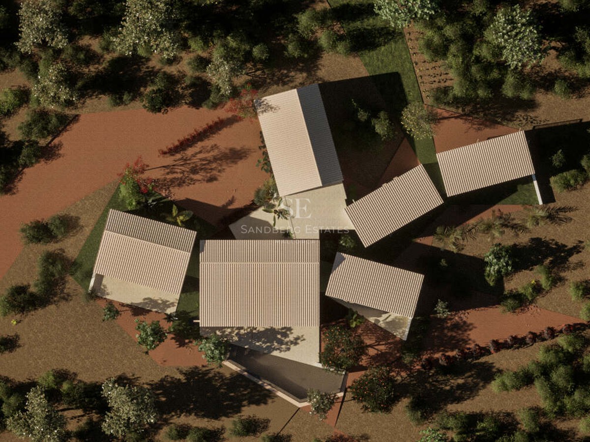 Bird's eye view of a contemporary villa with multiple pitched roofs surrounded by dense green Mediterranean trees.