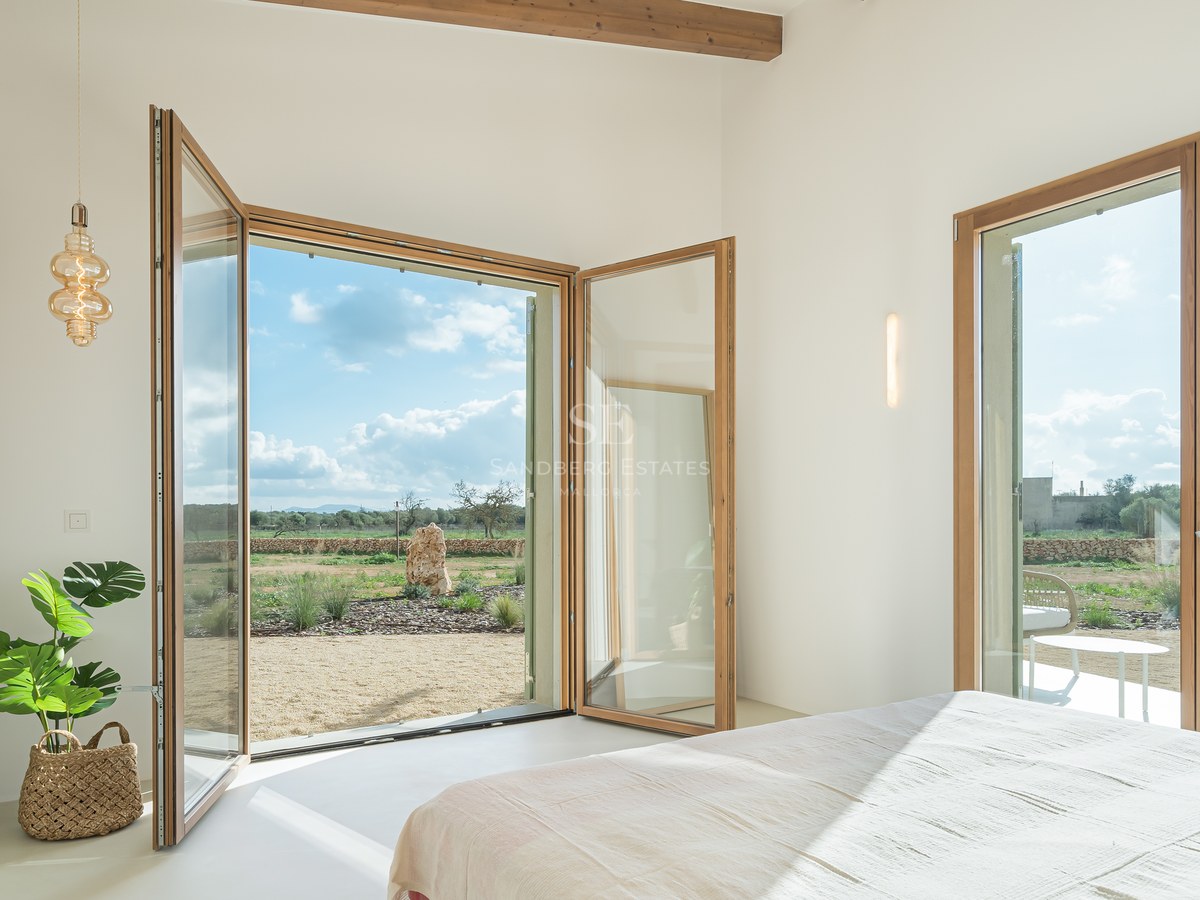 Bright bedroom featuring large wood-framed glass doors opening onto a Mediterranean landscape with olive trees.