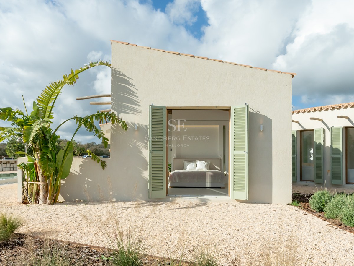 Exterior view of a minimalist sand-colored villa with sage green shutters opening into a bright master bedroom.