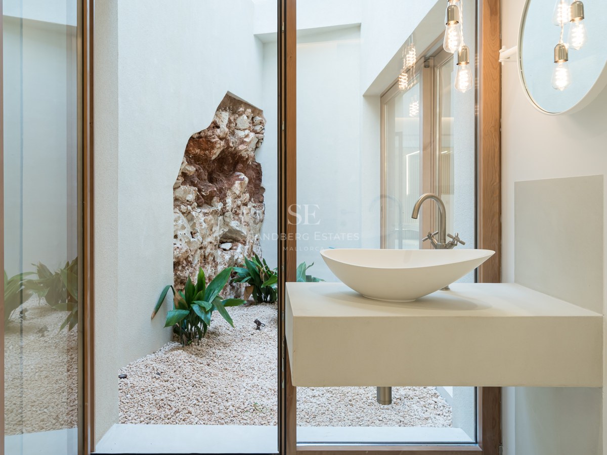 Modern vessel sink on a floating vanity looking through a glass wall at an internal courtyard with a natural stone feature.