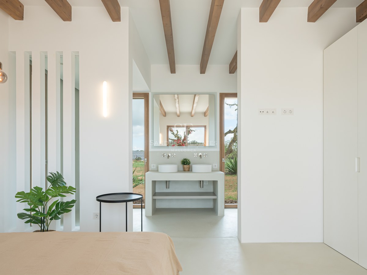 Minimalist master bedroom featuring white walls, exposed wooden beams, and an integrated ensuite vanity area.