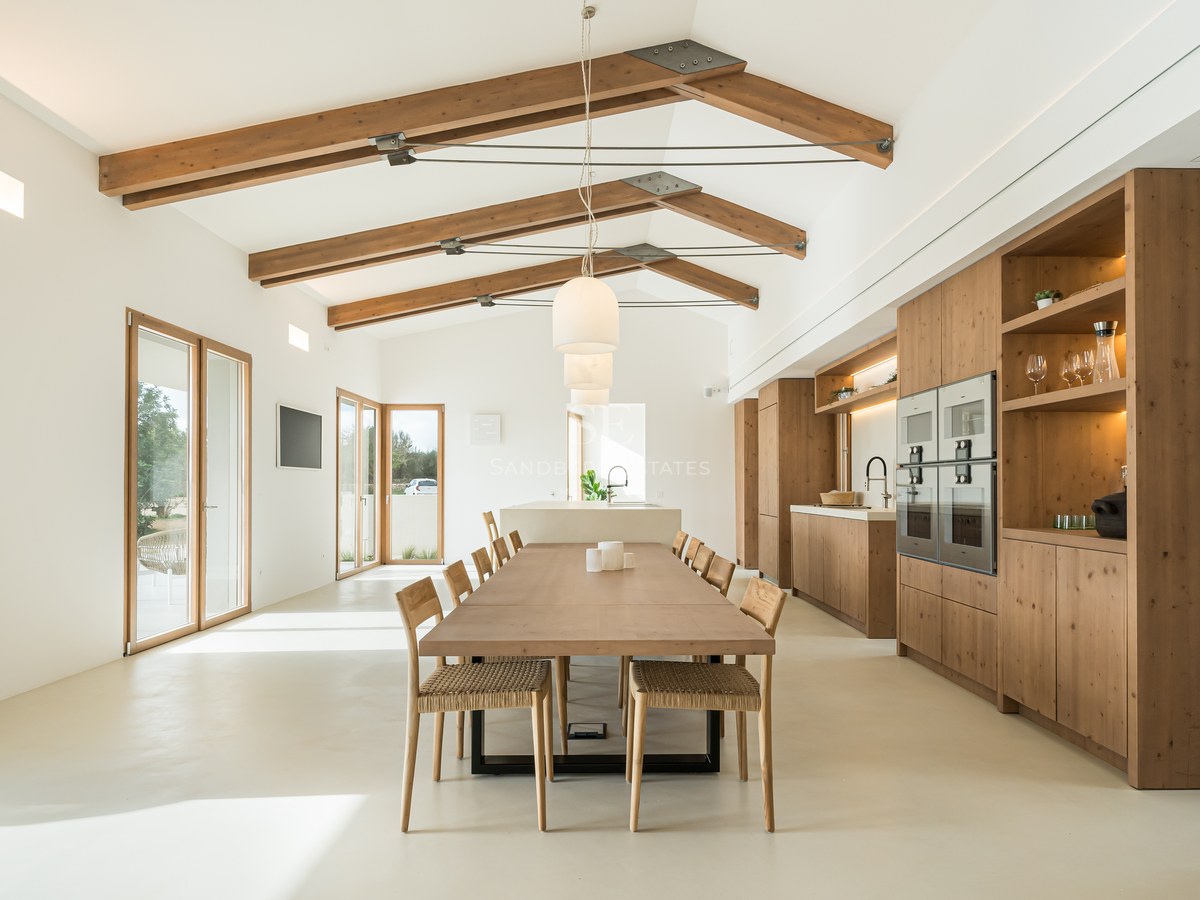 Bright open-plan dining room with vaulted ceilings, exposed wooden beams, and a large oak table next to a modern kitchen.