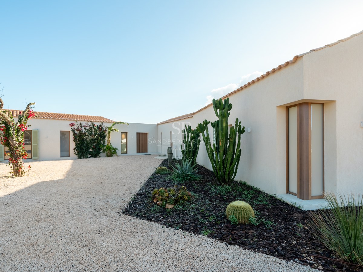 White contemporary villa with terracotta roof and a gravel courtyard featuring cacti and bougainvillea under a blue sky.