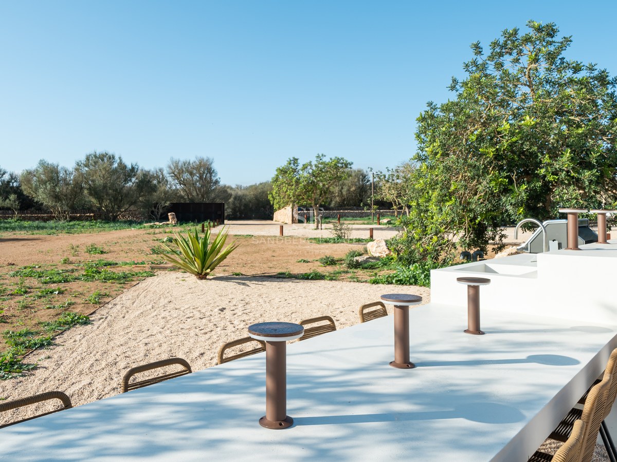 Minimalist white outdoor bar with integrated seating overlooking a Mediterranean landscape with trees and gravel.