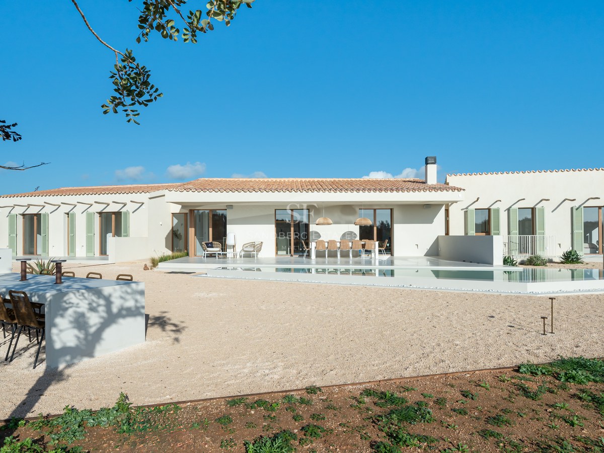 Wide shot of a beige one-story villa featuring a turquoise pool, outdoor kitchen, and green shutters under a blue sky.