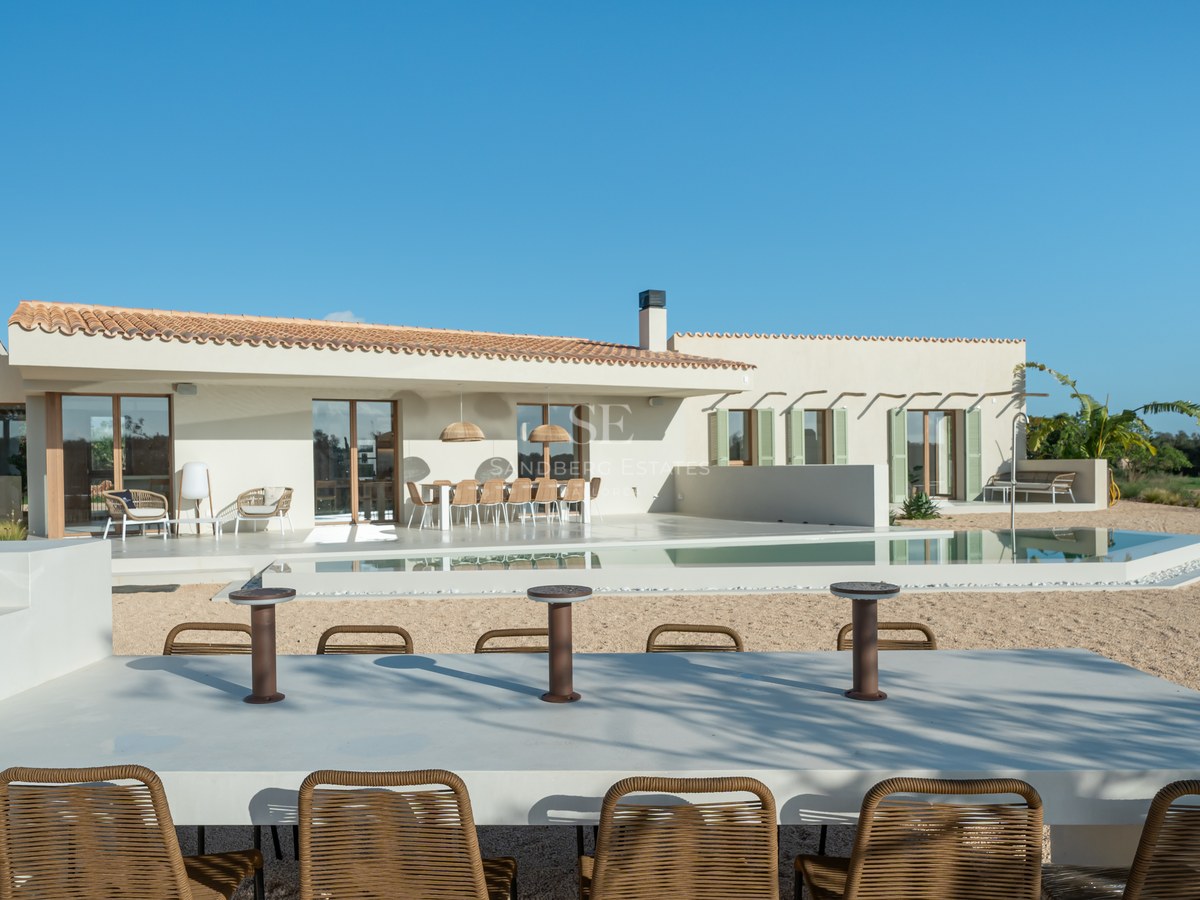 Single-story sand-colored villa with a swimming pool, multiple outdoor seating areas, and a clear blue sky.