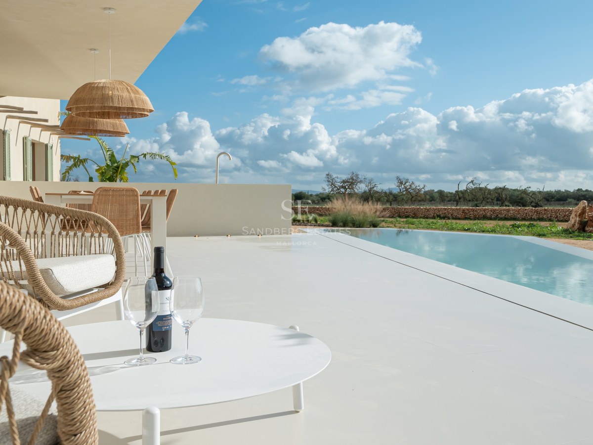 Luxury terrace with white microcement flooring, infinity pool, and woven furniture overlooking a Mediterranean landscape.