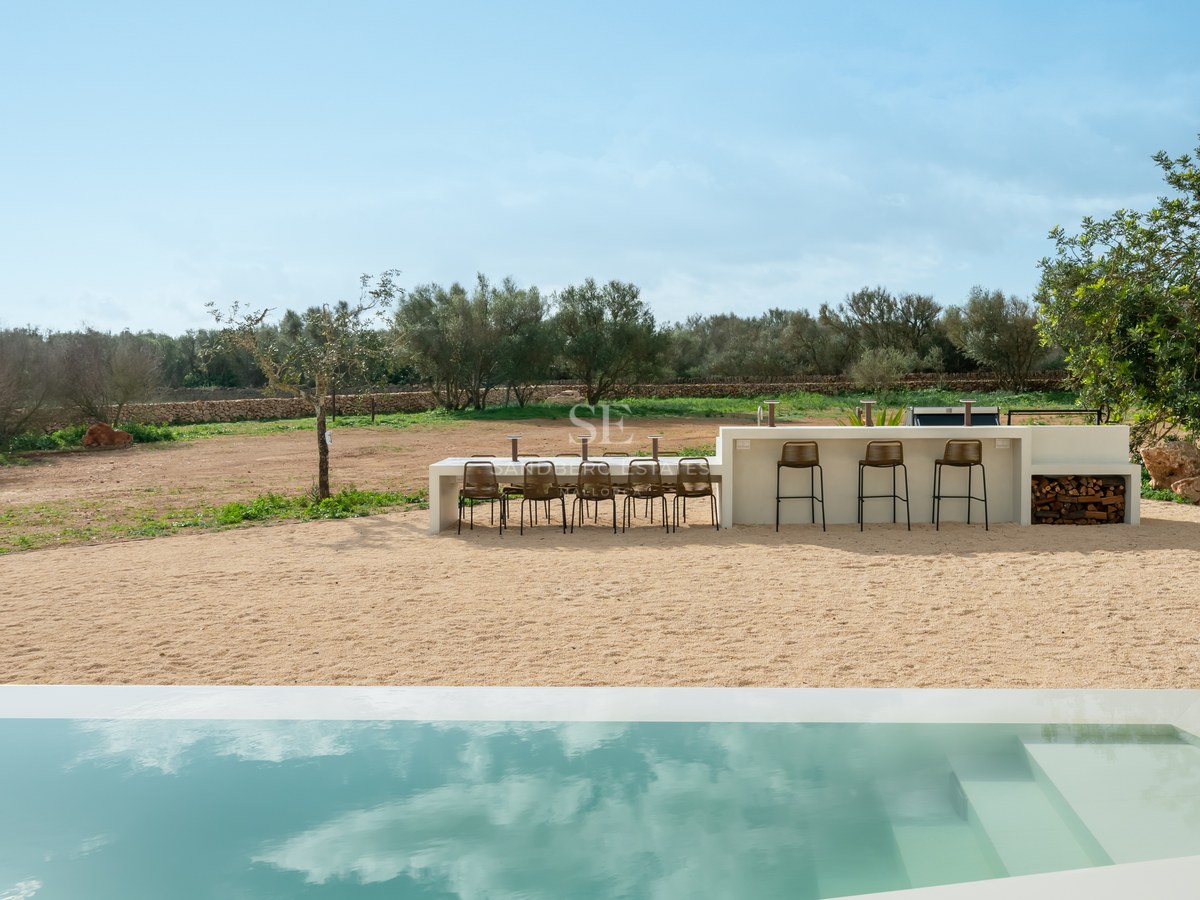 Modern white outdoor kitchen and dining area next to a sleek rectangular pool with Mediterranean landscape views.