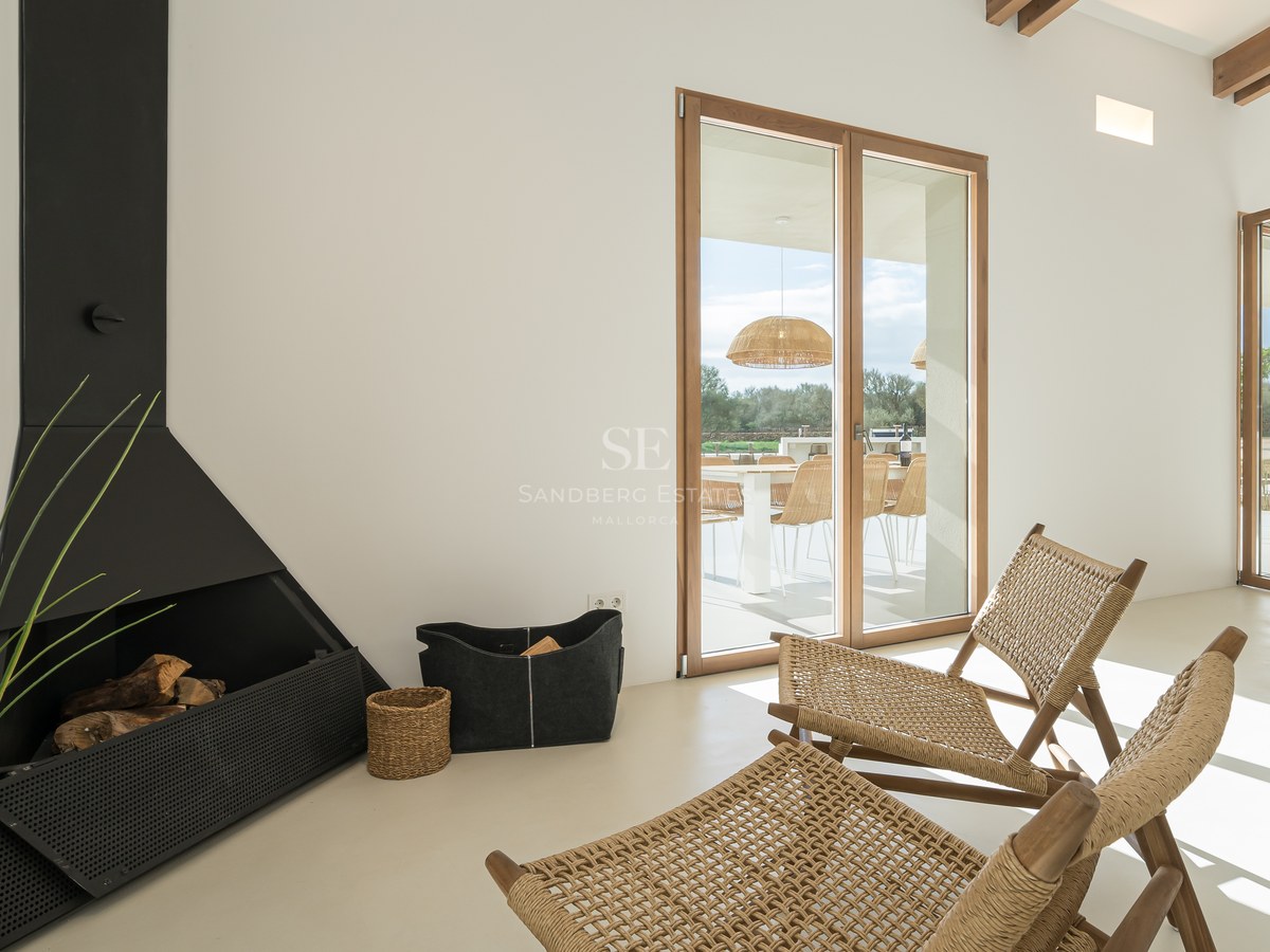 Minimalist interior featuring a sleek black fireplace, woven rattan chairs, and large wooden-framed glass doors to a terrace.