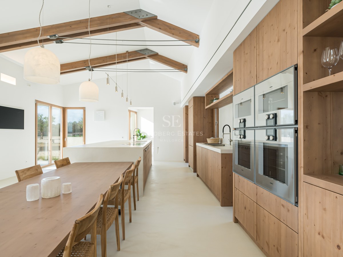 Bright open-plan kitchen and dining area with high vaulted ceilings, exposed wooden beams, and natural oak cabinetry.