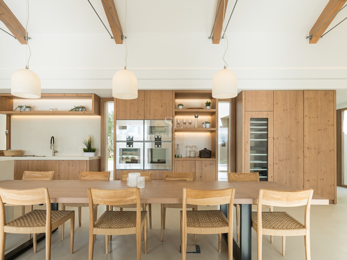 Light wood dining table with woven chairs in front of a modern oak kitchen featuring integrated appliances and wine cooler.