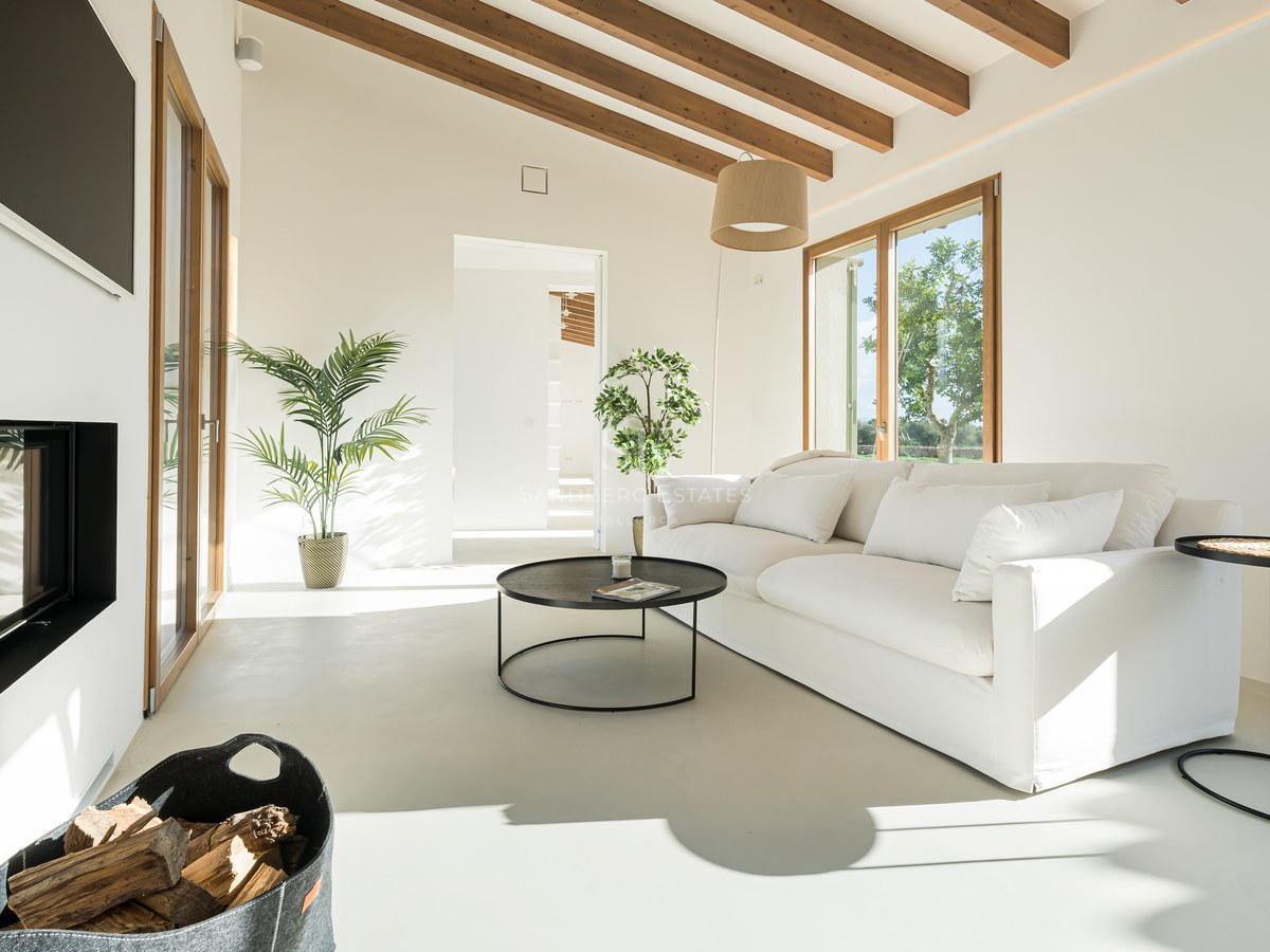 Minimalist living room with white sofa, wooden ceiling beams, modern fireplace, and floor-to-ceiling windows.