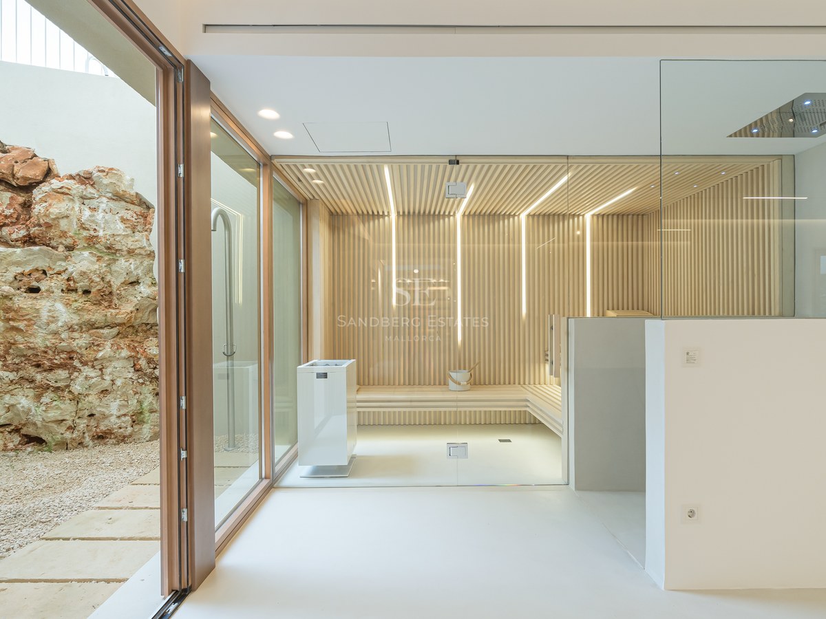 Modern wellness area featuring a slatted wood sauna, integrated shower, and views of a natural rock wall in a private courtyard.