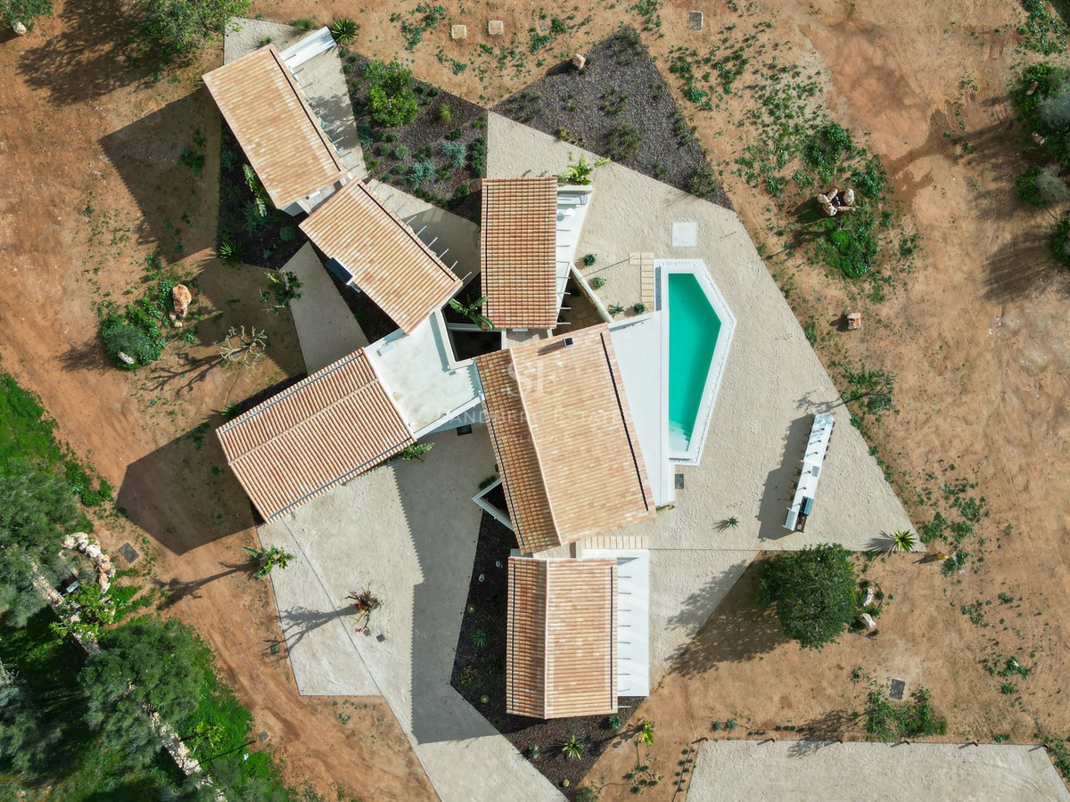 Birds-eye view of a modern villa with terracotta roofs and a turquoise pool set in a natural landscape.