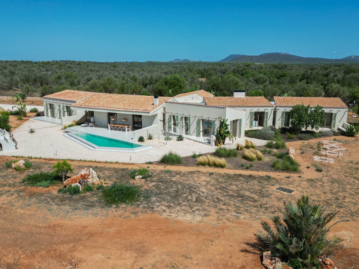 Aerial view of a modern single-story villa with terracotta roofs, geometric pool, and expansive natural landscape.