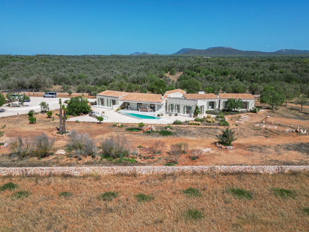 Aerial view of a modern white finca with terracotta roof and swimming pool surrounded by vast rural landscape.