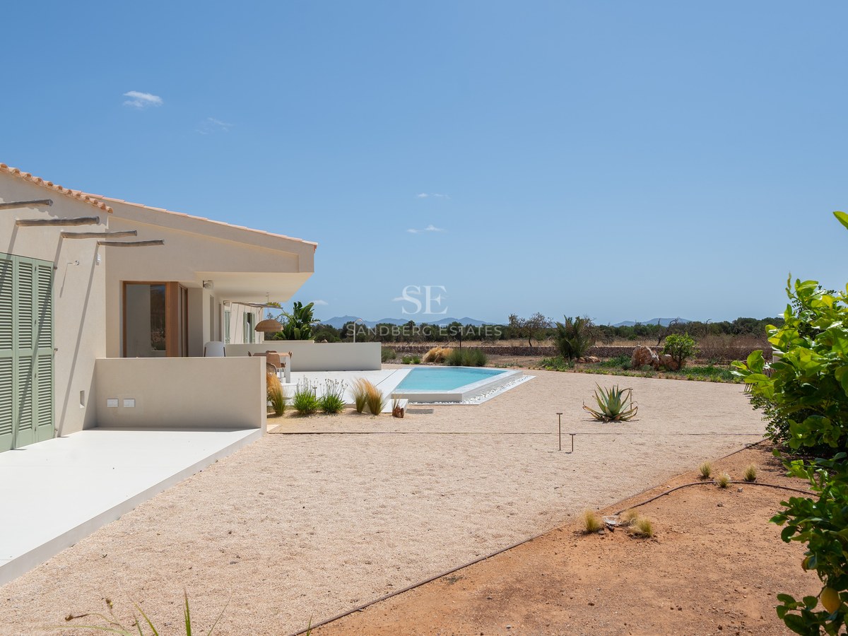 Modern beige villa with green shutters, a turquoise pool, and mountain views under a clear blue sky in Mallorca.
