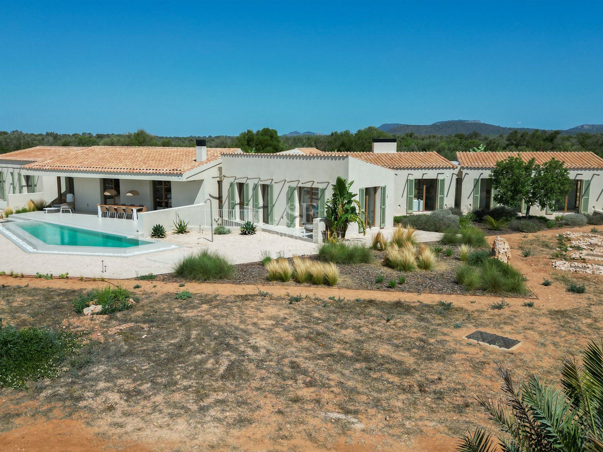 Aerial view of a luxury single-story villa with a pool, terracotta roof, and green shutters in a desert landscape.
