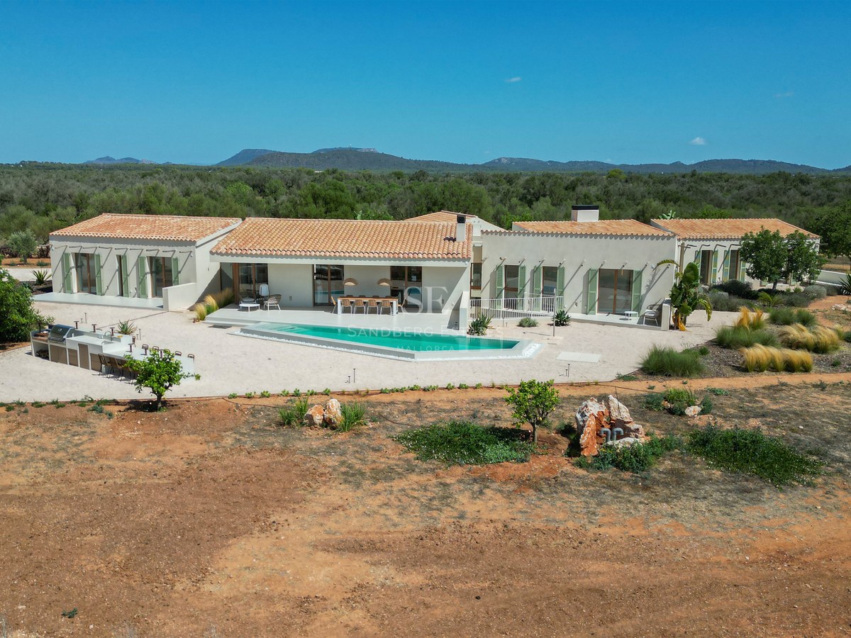 Elevated view of a modern single-story villa with a turquoise pool, outdoor kitchen, and terracotta roof in Mallorca.