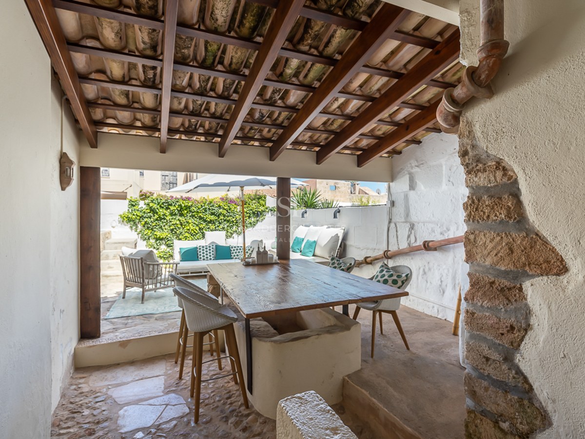 Überdachte mediterrane Terrasse mit großem Holztisch, Sichtbalken und hellem Außen-Loungebereich.