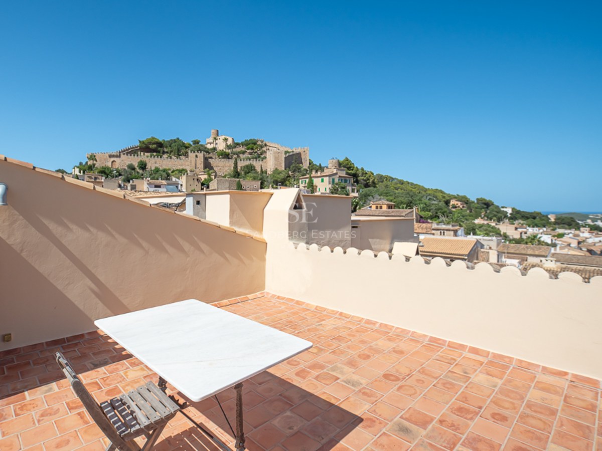 Dachterrasse mit Terrakottafliesen und Marmortisch, mit Blick auf eine historische Burg auf einem grünen Hügel.