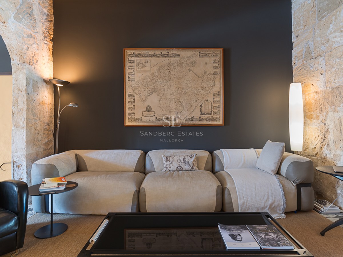 Modernes beiges Sofa vor anthrazitfarbener Wand mit Mallorca-Karte und freigelegten Natursteinbögen.