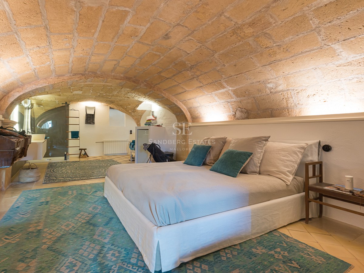 Schlafzimmer mit Sandsteingewölbe, weißen Wänden, türkisfarbenen Teppichen und modernem Bett.