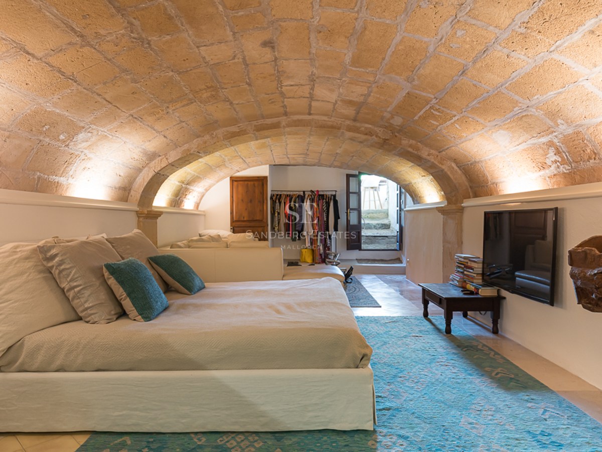 Schlafzimmer mit niedrigem Sandsteingewölbe, großem Bett mit türkisfarbenen Kissen und indirekter Beleuchtung.