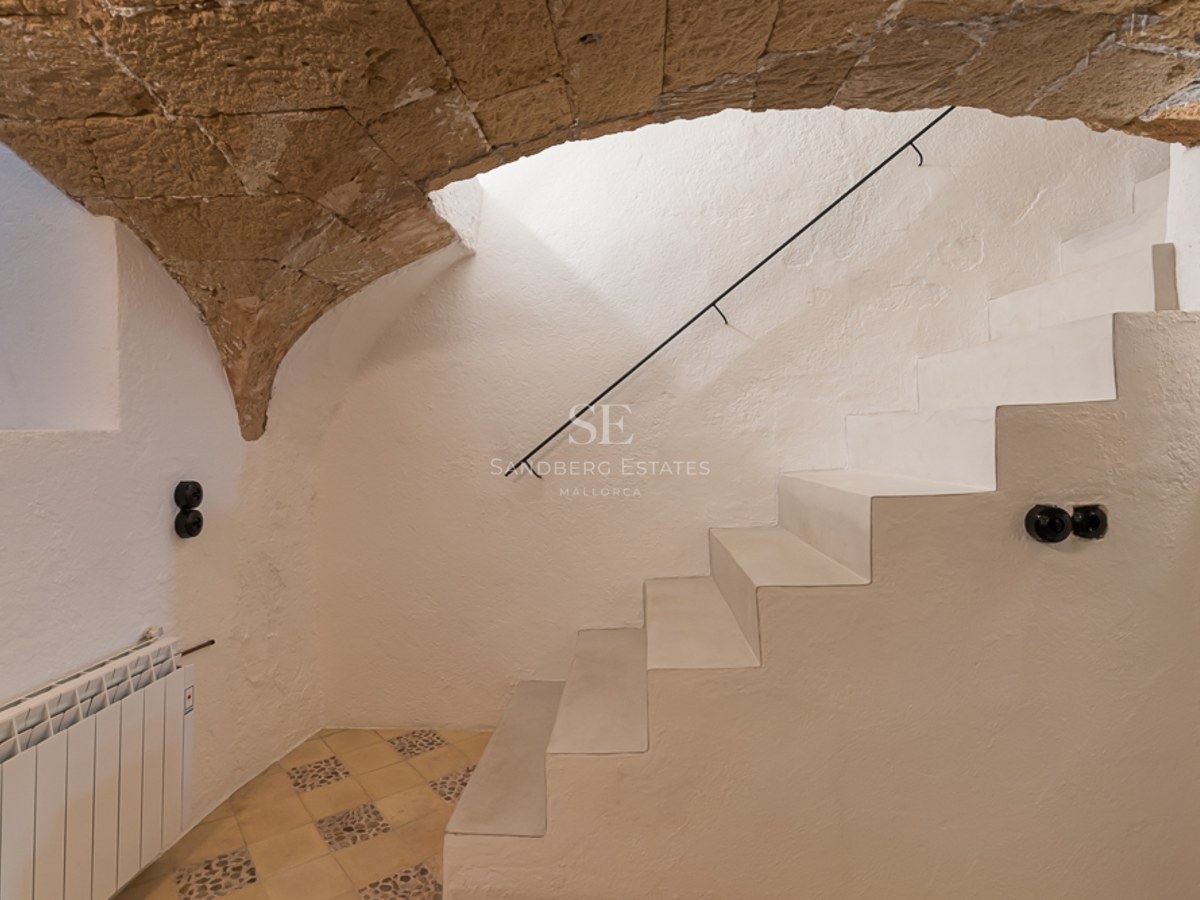 Minimalistische weiße Treppe unter einem Natursteinbogen in einem renovierten Stadthaus auf Mallorca.