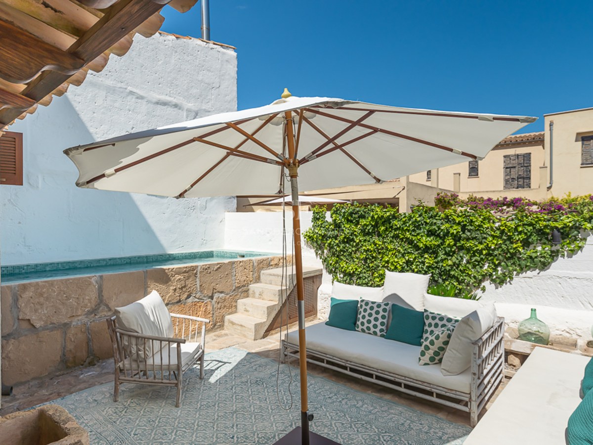 Sonniger mediterraner Innenhof mit erhöhtem Steinpool, weißem Sofa und großem Sonnenschirm.