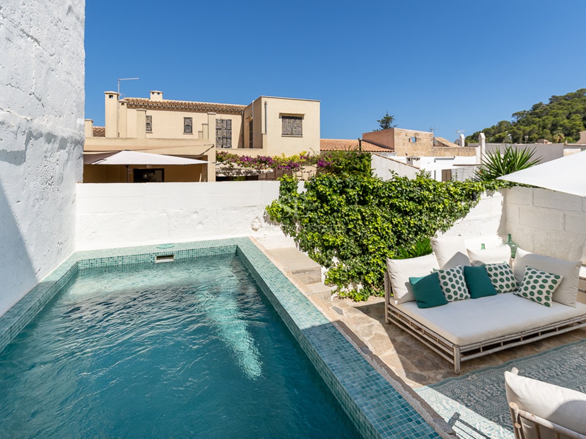 Privater türkisfarbener Pool in einem Innenhof mit weiß getünchten Wänden, Steinboden und Loungemöbeln.