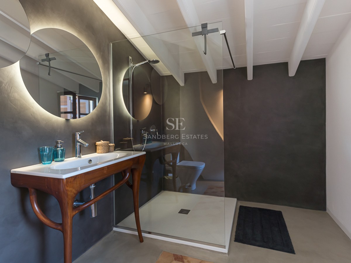 Modernes Badezimmer mit dunkelgrauen Mikrozementwänden, rundem beleuchtetem Spiegel und Holzwaschtisch.