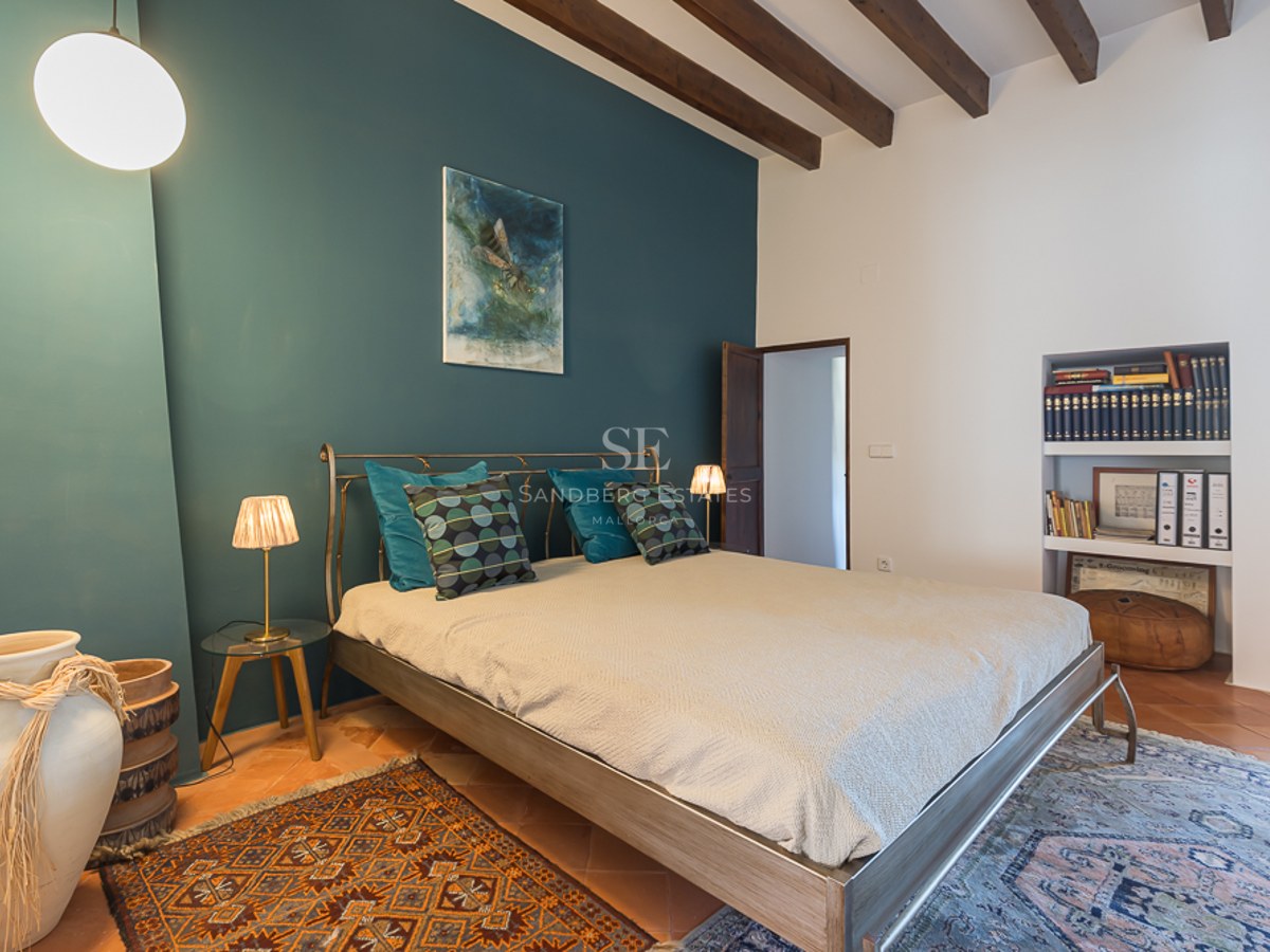 Schlafzimmer mit petrolfarbener Wand, Holzbalkendecke, Terrakottaboden und Metallbett.