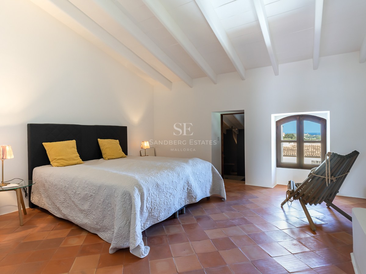 Schlafzimmer mit weißer Balkendecke, Terrakottaboden, großem Bett und Rundbogenfenster mit Blick auf das Meer.