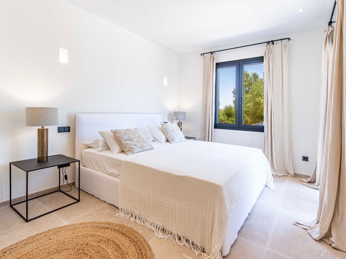 Chambre lumineuse avec lit double, sol en pierre naturelle, tapis en jute et vue sur les arbres.